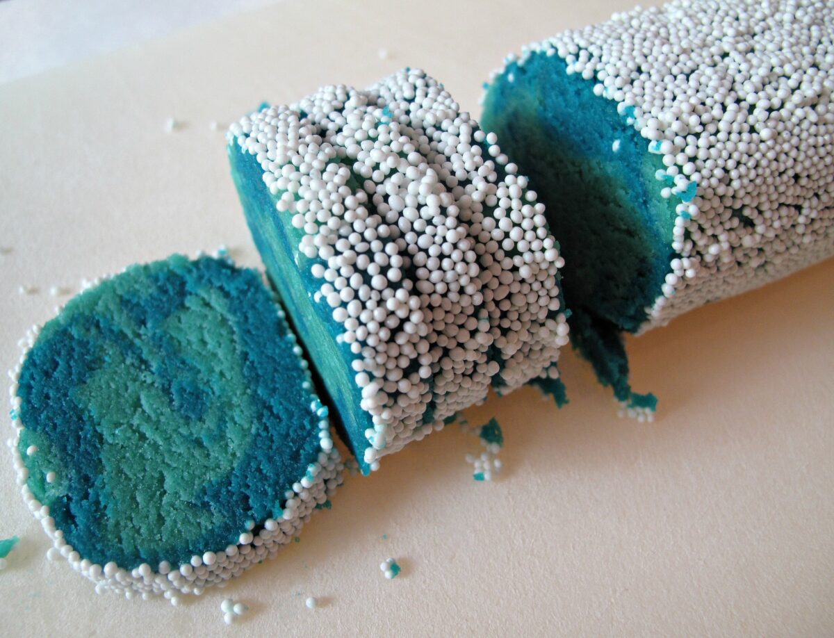 Sliced log of blue sugar cookie dough coated in white nonpareil sprinkles.