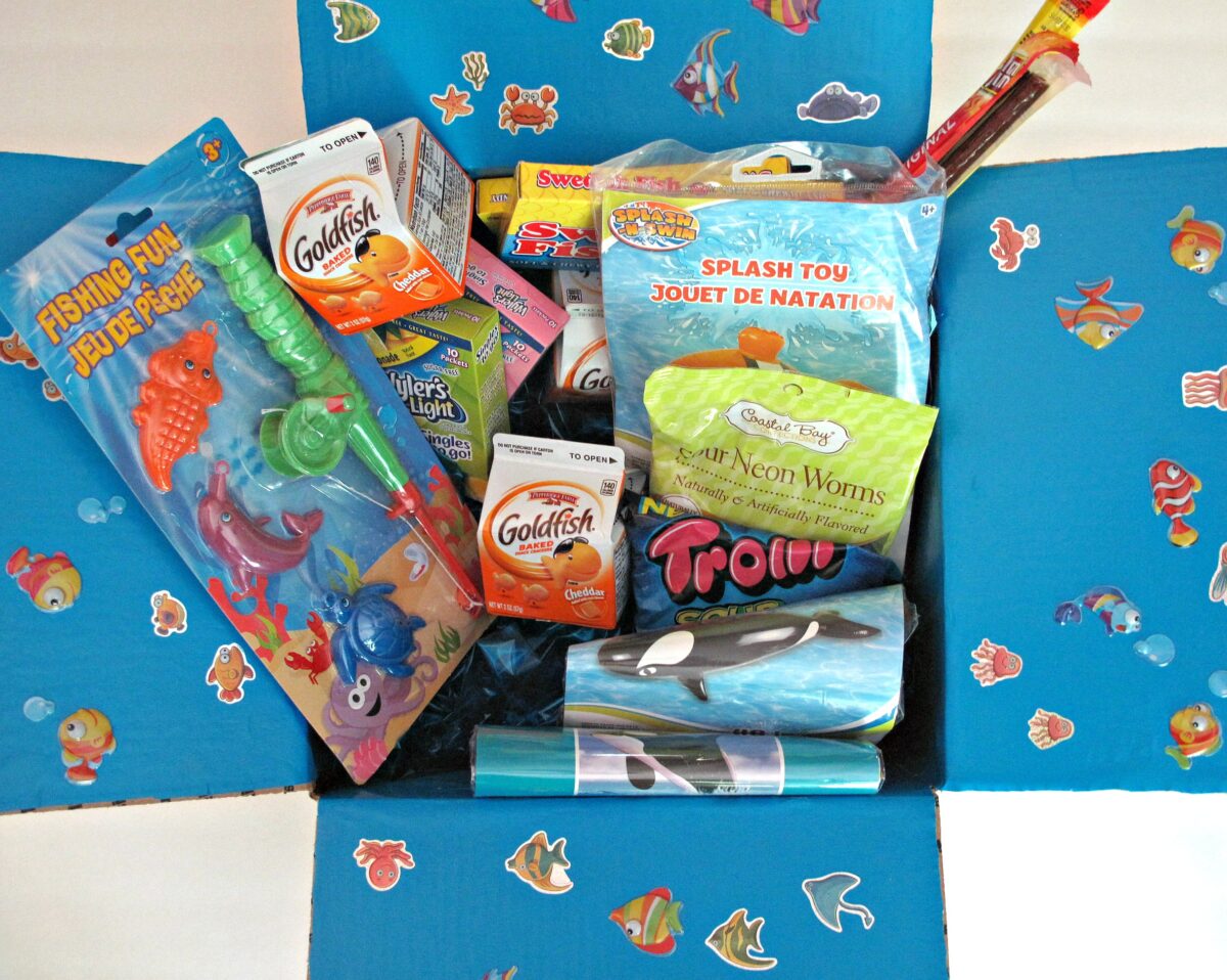 Filled Fishing Care Package with box flaps decorated with blue paper and fish stickers.