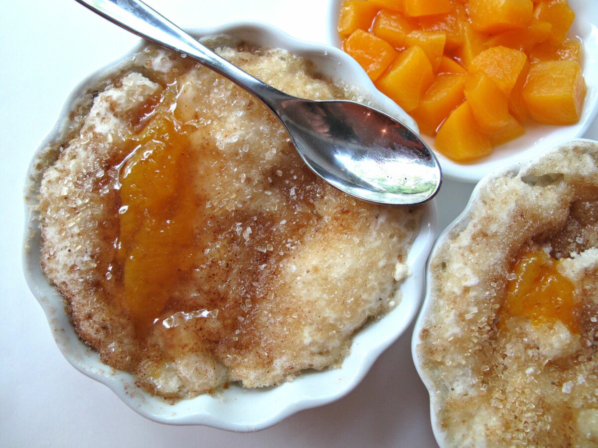 Individual servings of microwave peach cobbler with a spoon.