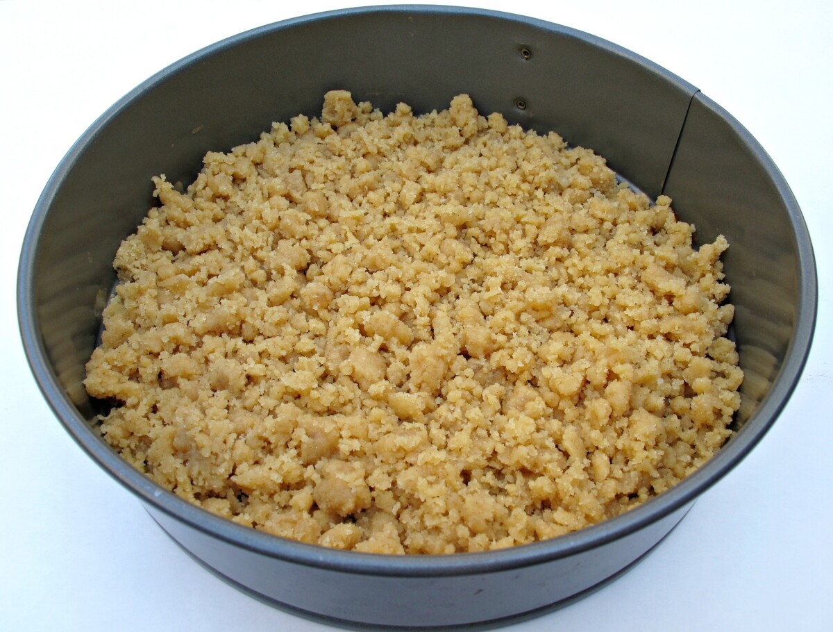 Streusel crumbs packed into the bottom of a round springform cake pan.