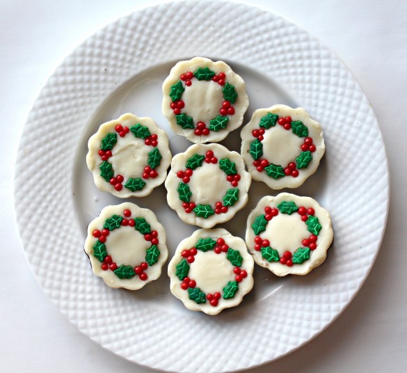 Pieces of Christmas Wreath Fudge on a white plate. Each piece of fudge is white chocolate on the top and milk chocolate on the bottom and is decorated with green holly leaf sprinkles and red berry sprinkles.