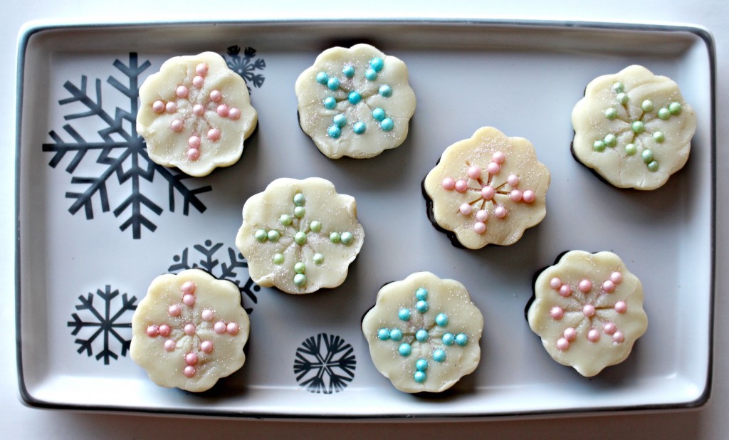 Pieces of Snowflake Fudge on a platter. Each piece is white chocolate on the top and milk chocolate on the bottom. The top is decorated with pastel colored nonpareils in a criss cross pattern to resemble a snowflake.