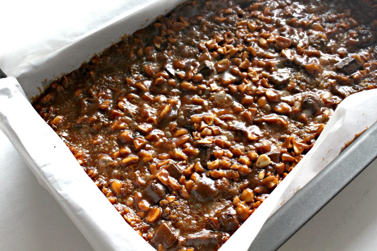 Baking pan lined with parchment filled with chocolate chip peanut caramel bar batter.