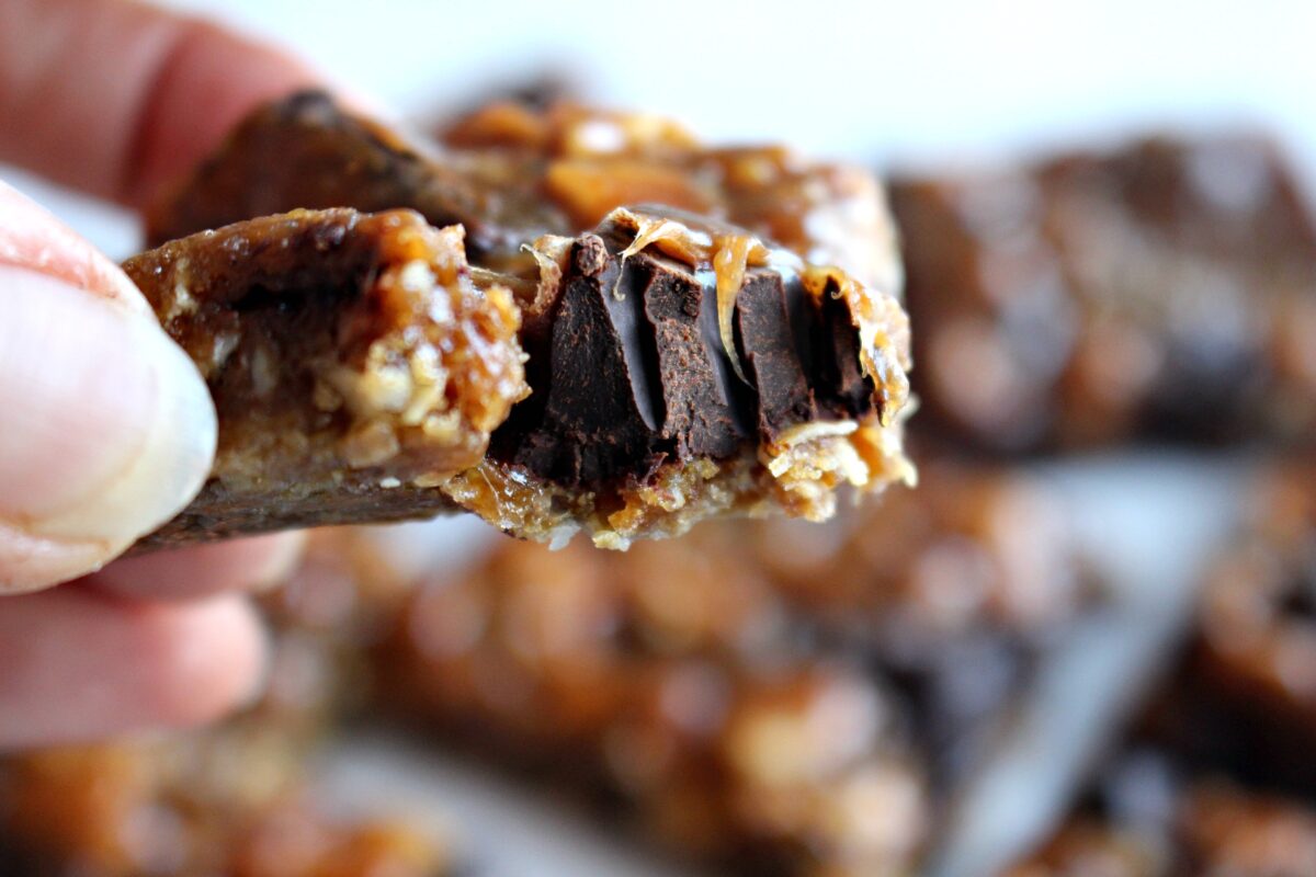 Caramel Chocolate Peanut Bars with a bite missing and a chunk of chocolate showing.