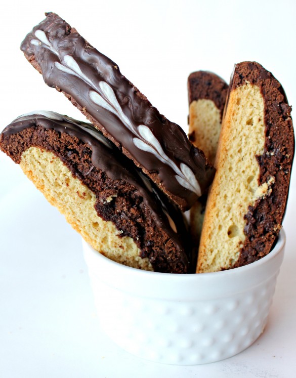 Black and White Biscotti in a white serving bowl showing closeup of chocolate and vanilla cookie layers and the top of a biscotti coated in dark chocolate with white chocolate hearts.