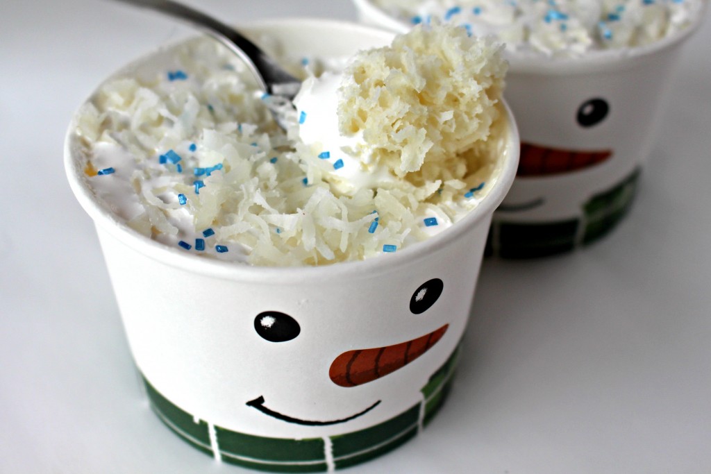A spoon scooping up some Coconut Snowball Mug Cake in a paper cup with a snowman face