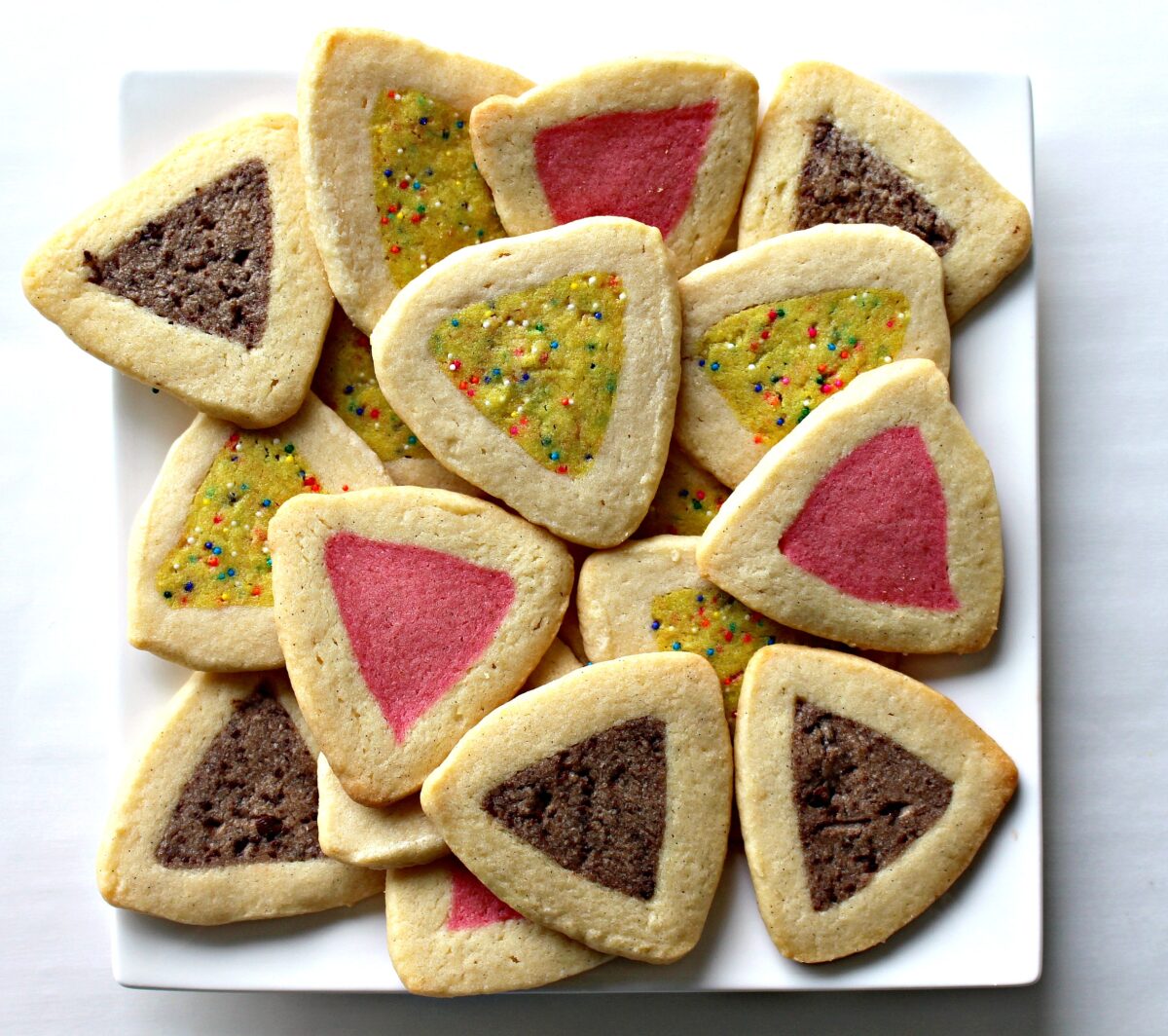 Triangle Hamantaschen, buttery sugar cookies with flavored and colored centers in brown, pink, and yellow.