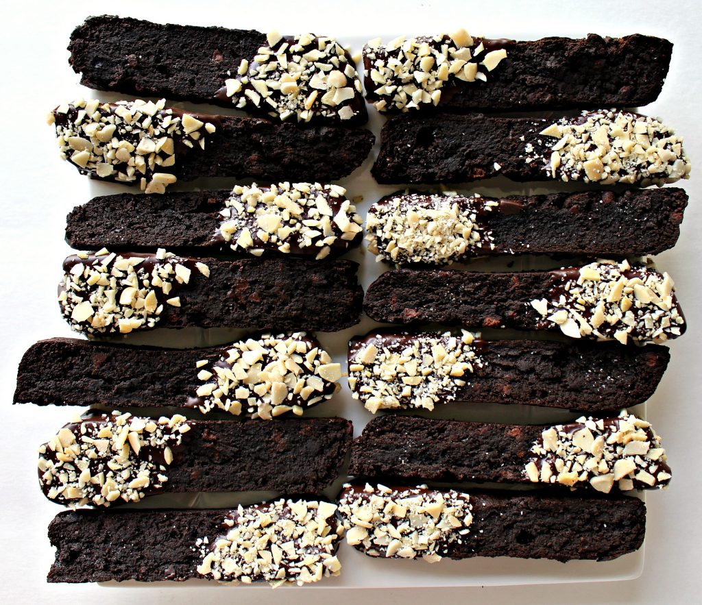 Double Chocolate Passover Biscotti (GF) with one end of each dipped in chocolate and chopped almonds on white plate.