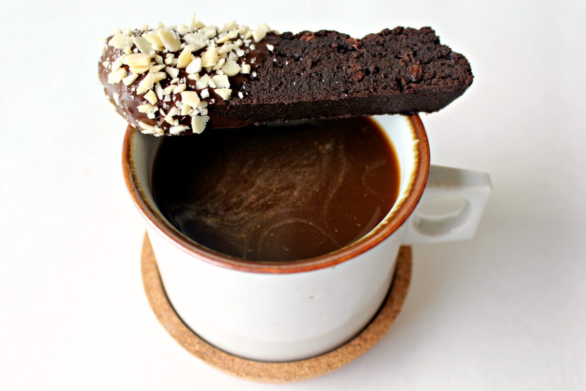 A chocolate biscotti balanced on the edge of a mug of coffee.