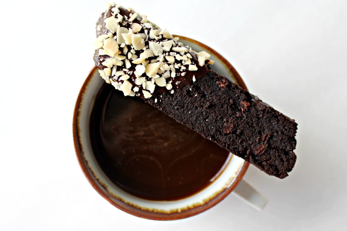 Overhead image of a chocolate biscotti balanced on rim of mug of coffee.