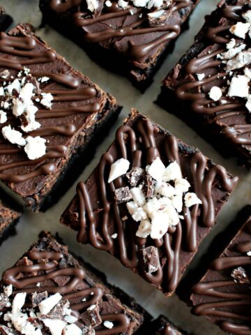 Coseup of chocolate brownie squares drizzled with chocolate and topped with chopped peppermint patties.