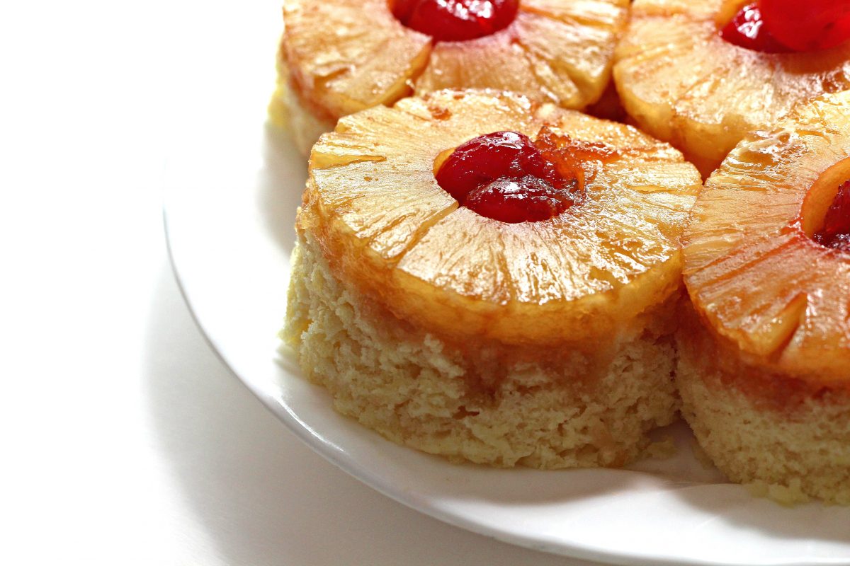 Closeup of one Pineapple Upside Down Cake in a mug with pineapple and cherries on top.
