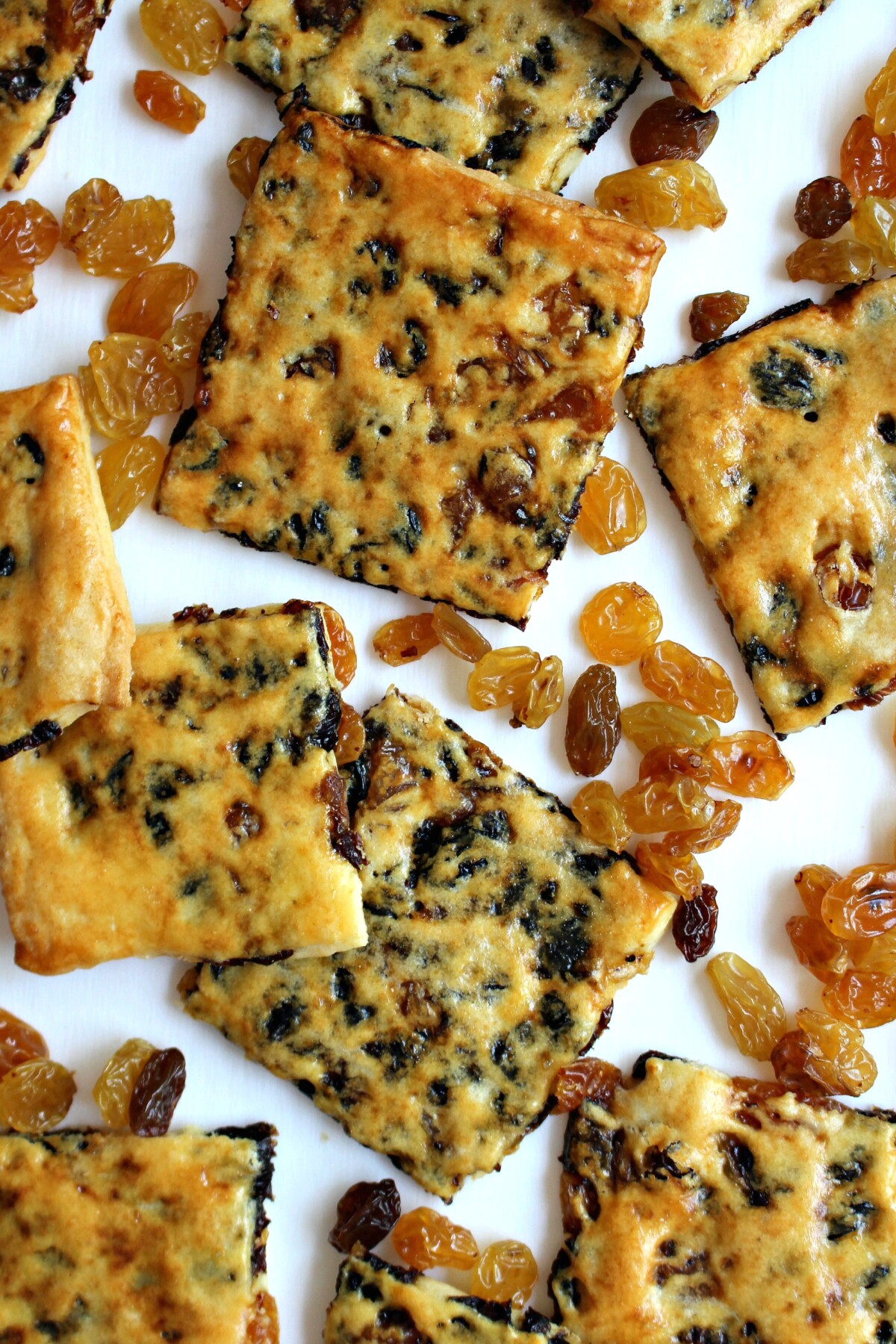 Thin cookie squares with raisins showing through the crust on a white background.