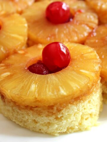 Closeup of pineapple slice and maraschino cherry on top of vanilla mug cake.