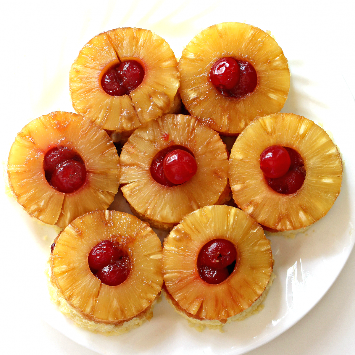 Overhead photo of 7 pineapple upside down mugs cakes on a serving platter.