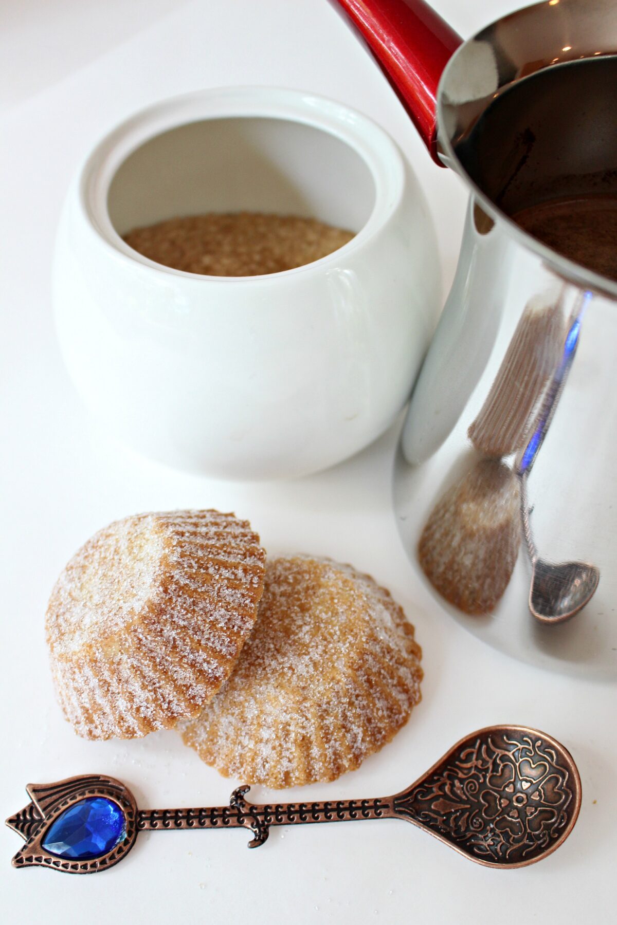 Two cookies with a Bosnian coffee pot, sugar bowl, and spoon.