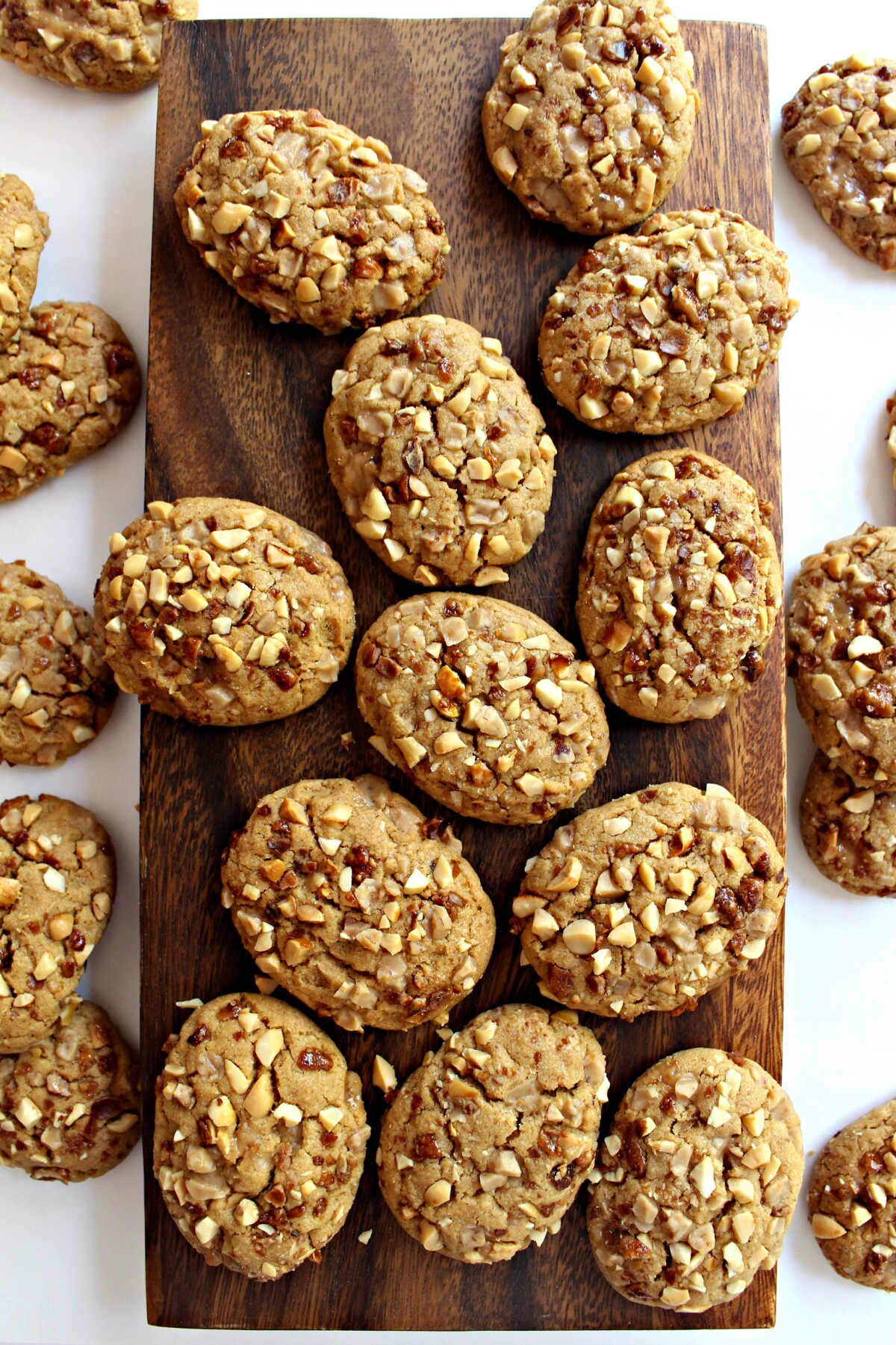 Toffee Peanut Cookies  coated in chopped peanuts, on a wooden cutting board.