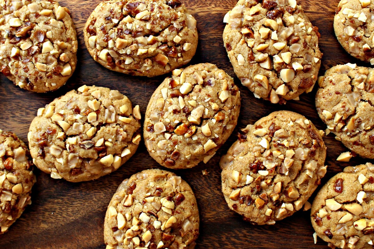 Closeup of oval shaped cookies coated in chopped peanuts and toffee bits on a wooden surface.
