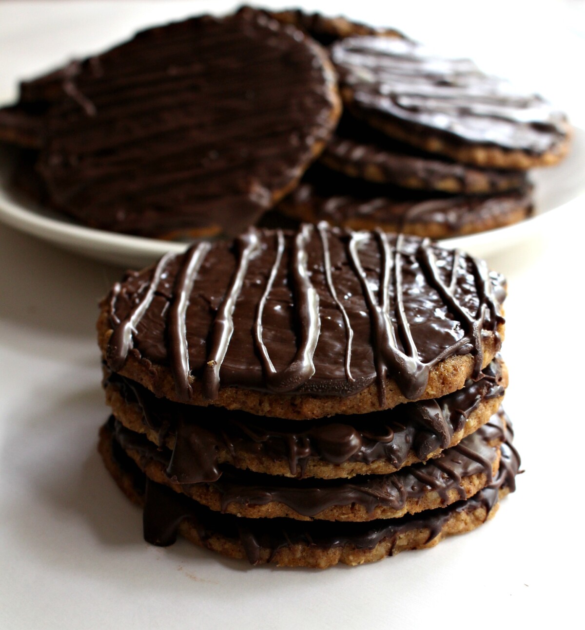 Four cookies in a stack and a white plate of cookies in the background.