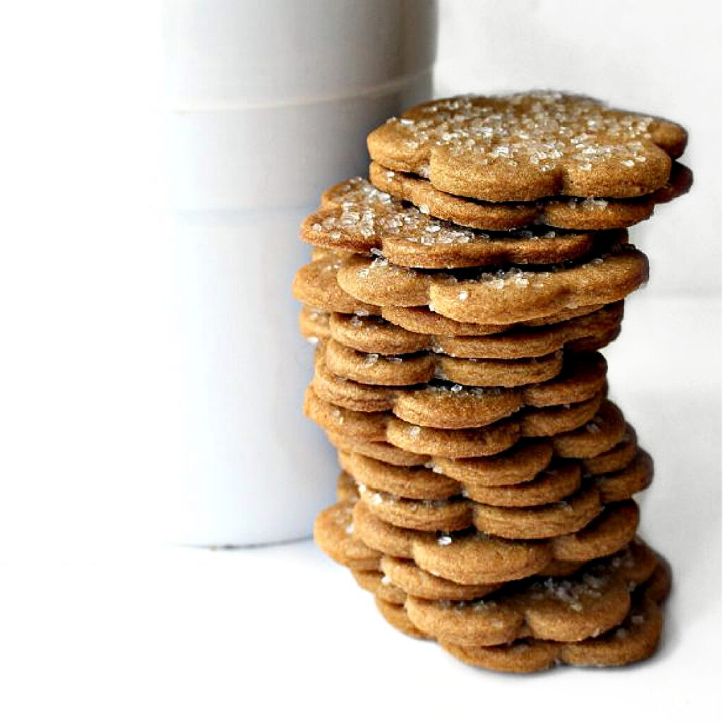 Stack of thin, small flower shaped cookies in front of a cookie jar.