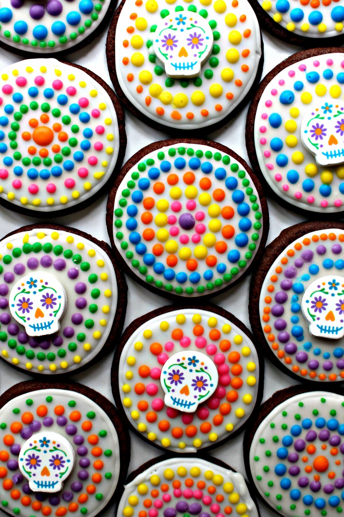 Chocolate sugar cookies decorated with white icing, colorful dot and sugar skulls.
