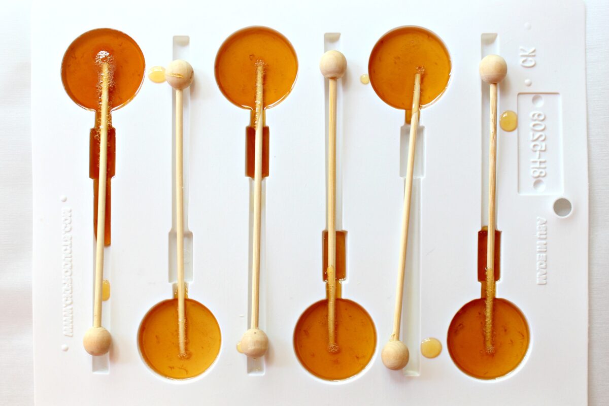 White plastic mold for circle lollipops filled with honey syrup and wooden lollipop sticks.