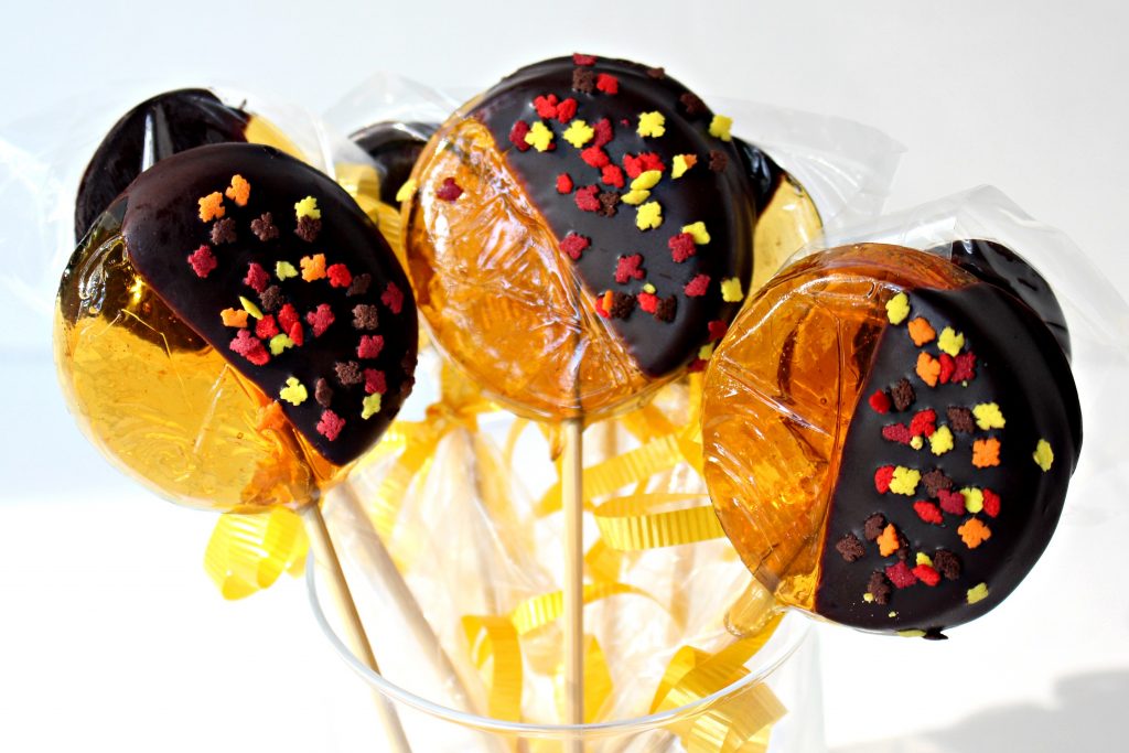 Lollipops dipped half in chocolate with tiny leaf sprinkles in fall colors.