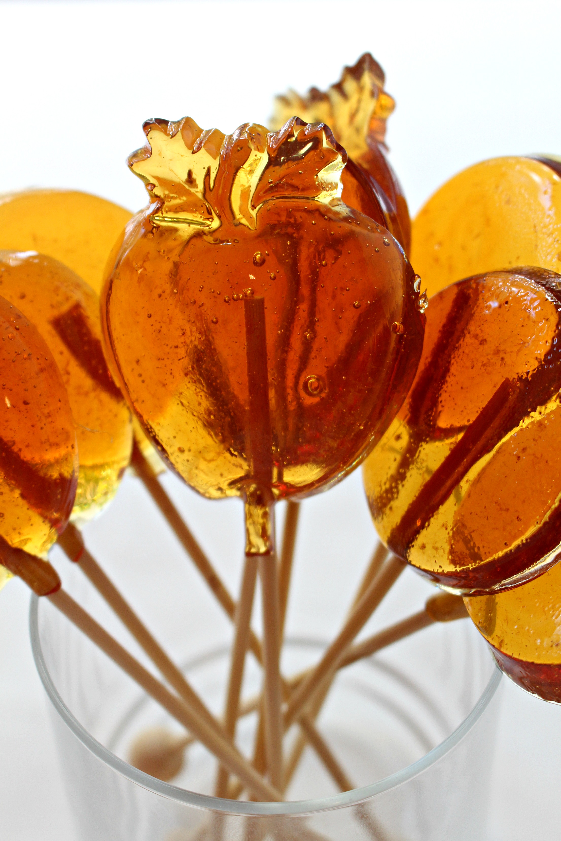 Amber colored Honey Lolipops molded in circle shapes and apple shape with wooden sticks.