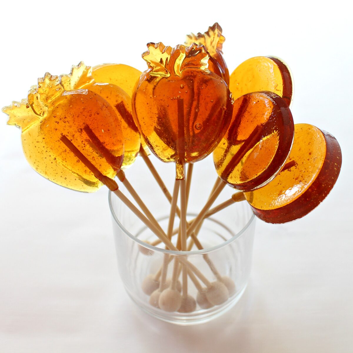 Apple and circle lollipops with wooden sticks in a clear glass.