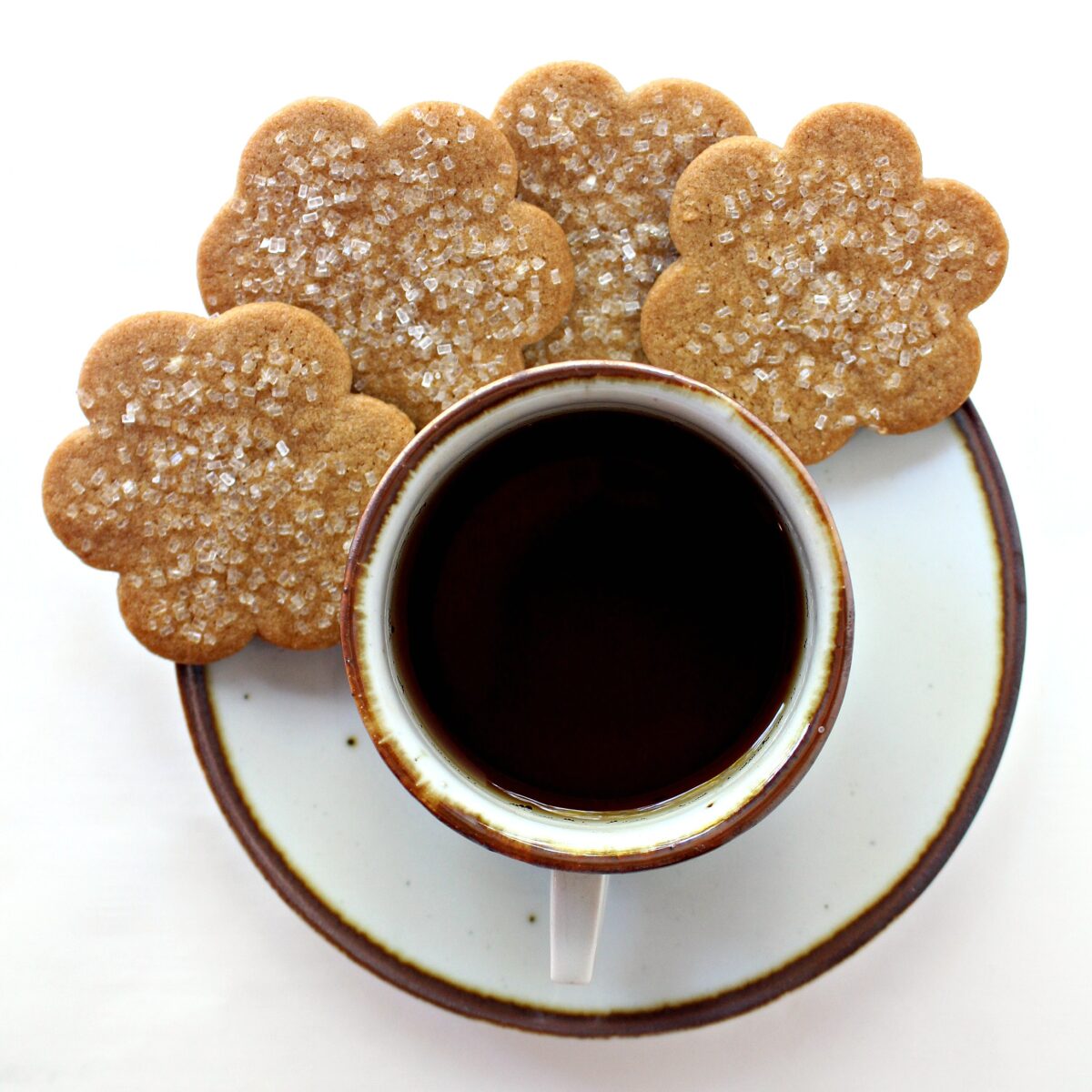 Overhead image of flower shaped cookie snaps on the saucer of a cup of tea.