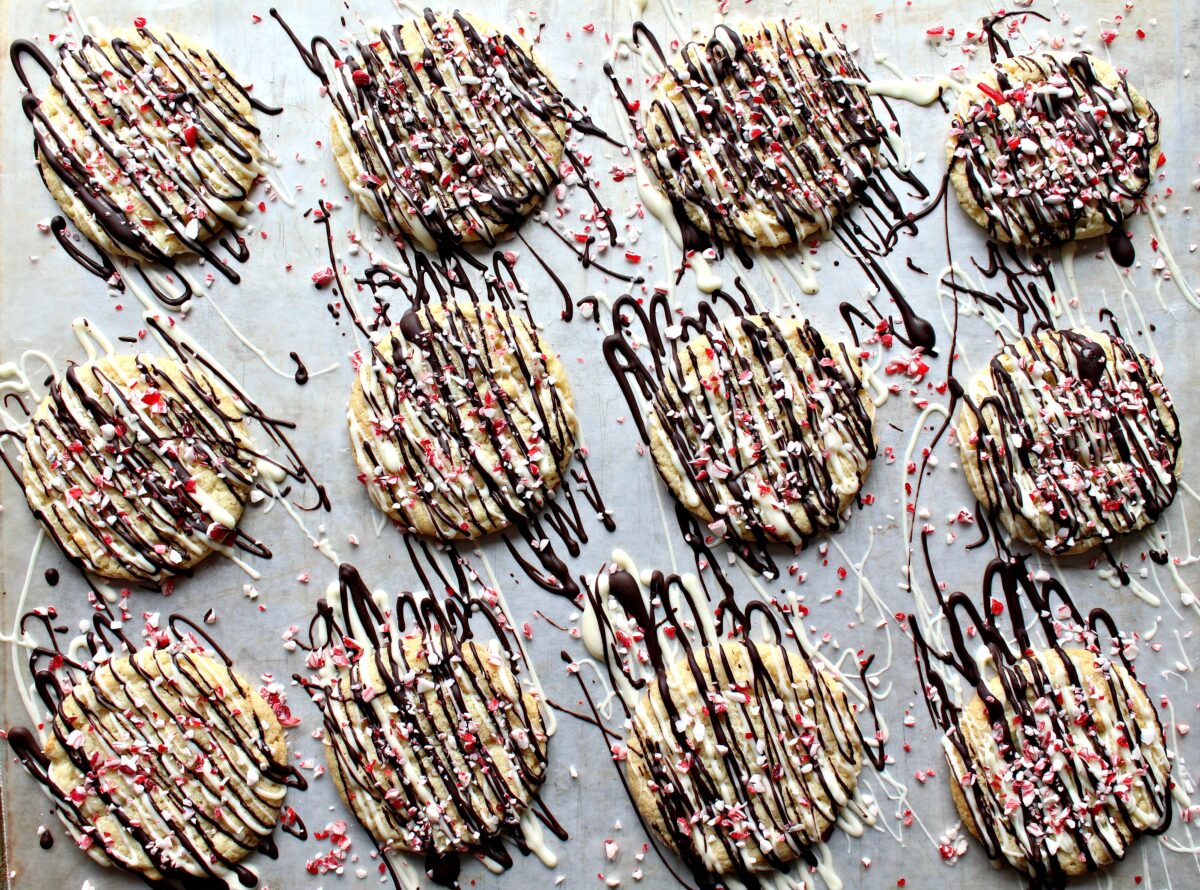 Cookies on wax paper with drizzles of white and dark chocolate and sprinkled with peppermint candy bits.