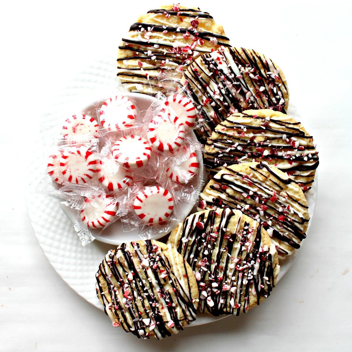  Cookies decorated with chocolate drizzles and candy bits on a white plate. 