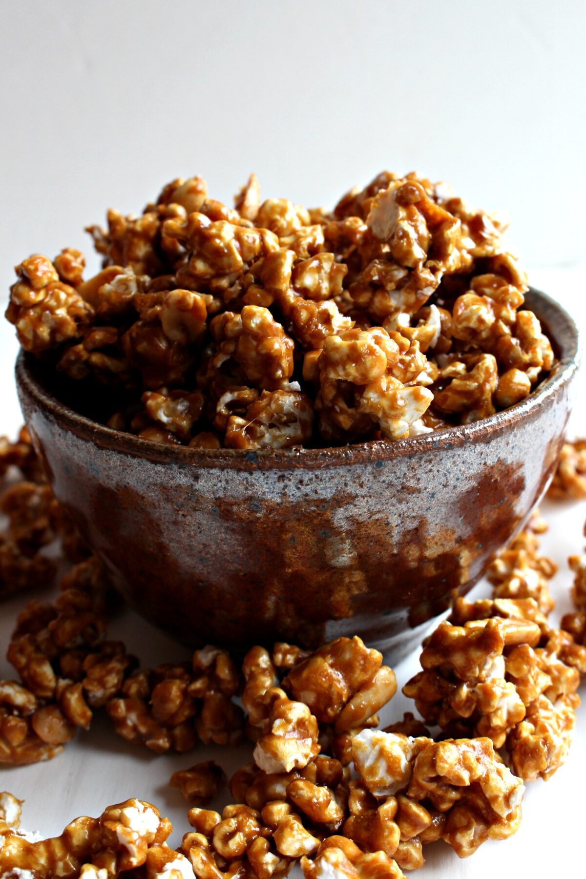 Caramel Popcorn with Peanuts, coated in a shiny, crisp coating, overflowing from a brown pottery serving bowl.
