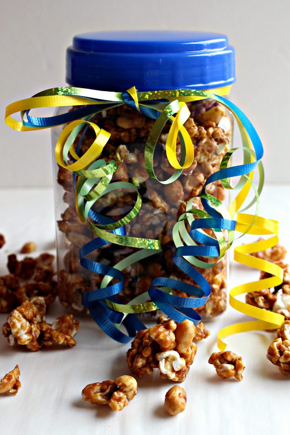 Caramel Popcorn with Peanuts ready for gifting in a clear jar with a blue lid and gold and blue ribbons.