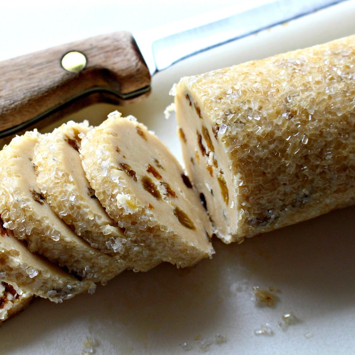 A roll of cookie dough coated un large crystal sugar being sliced.