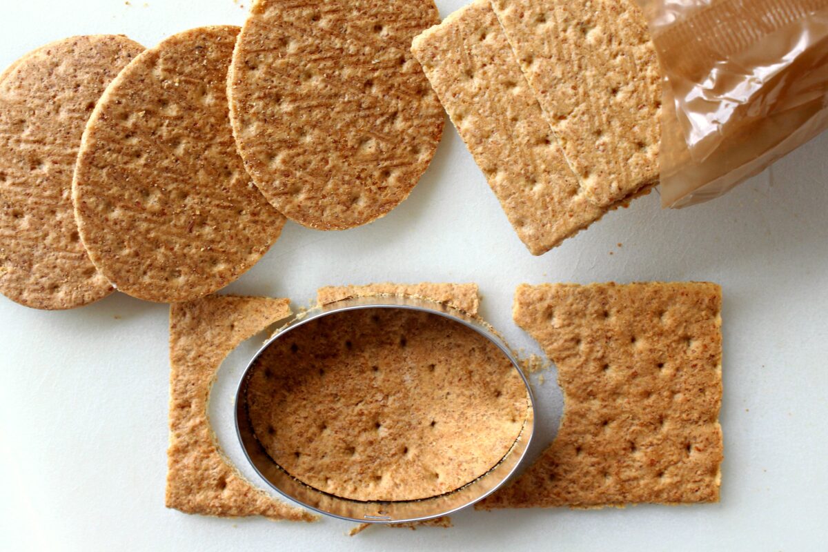  Graham crackers being cut into egg shapes with a cookie cutter.