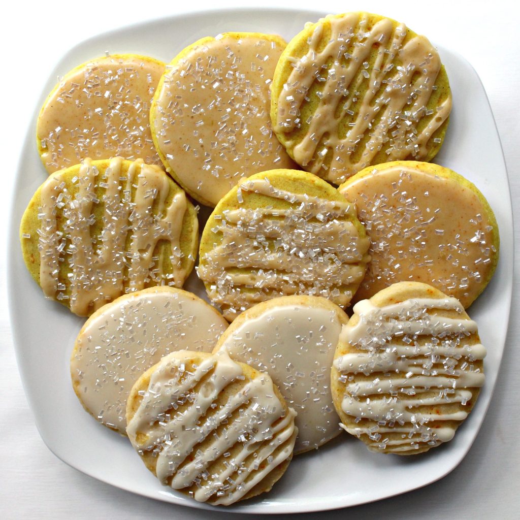 A plate of iced, round, flat Turmeric Cookies sprinked with decorating sugar.