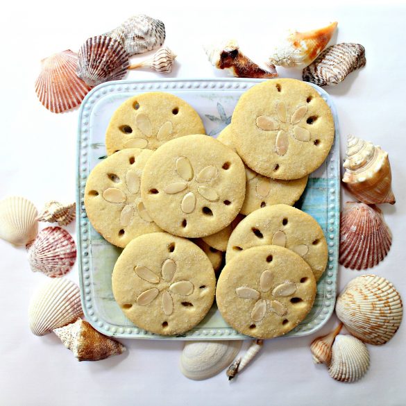 Almond Sand Dollar Cookies are almond flavored sugar cookies decorated to look like sand dollars with 5 holes around the edges and 5 almond slices in pressed into the center of each cookie in a flower formation.