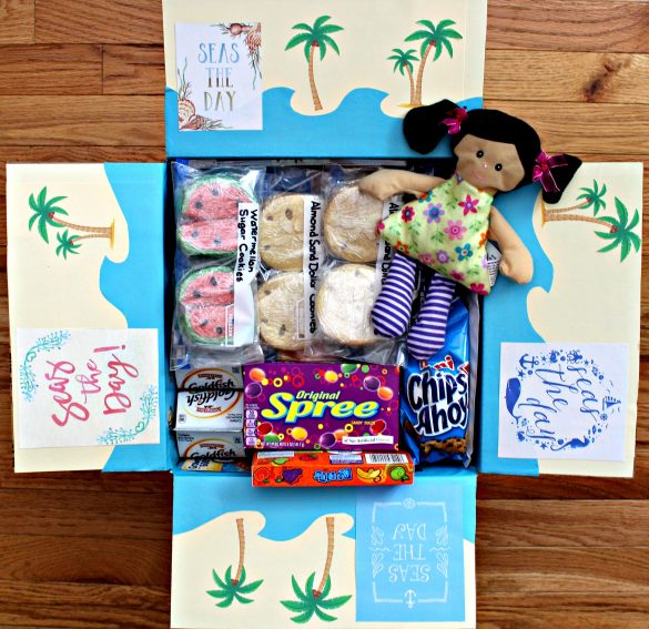 Seas the Day! A Day at the Beach care package with inside flaps decorated to look like the beach with blue paper waves and palm trees.