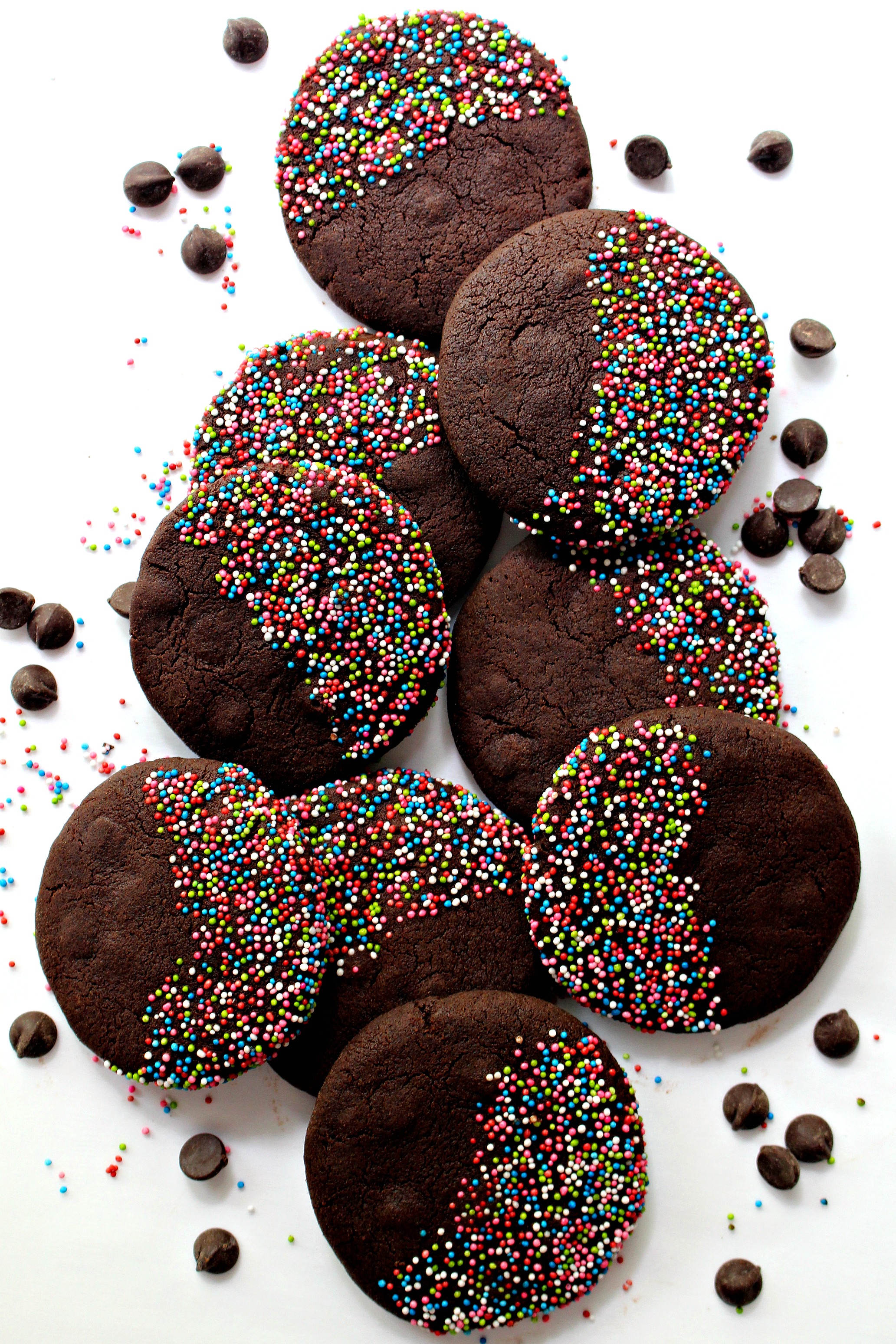 Dark chocolate brown cookies with multicolored nonpareil sprinkles covering half of the cookie top.