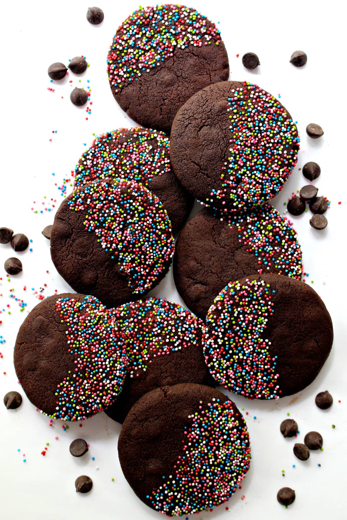 Dark chocolate brown cookies with multicolored nonpareil sprinkles covering half of the cookie top.