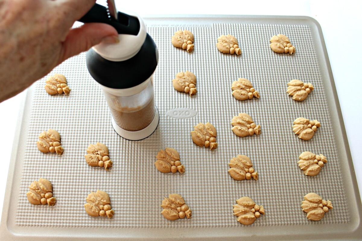 Using cookie press to add owl cookies to a baking sheet.