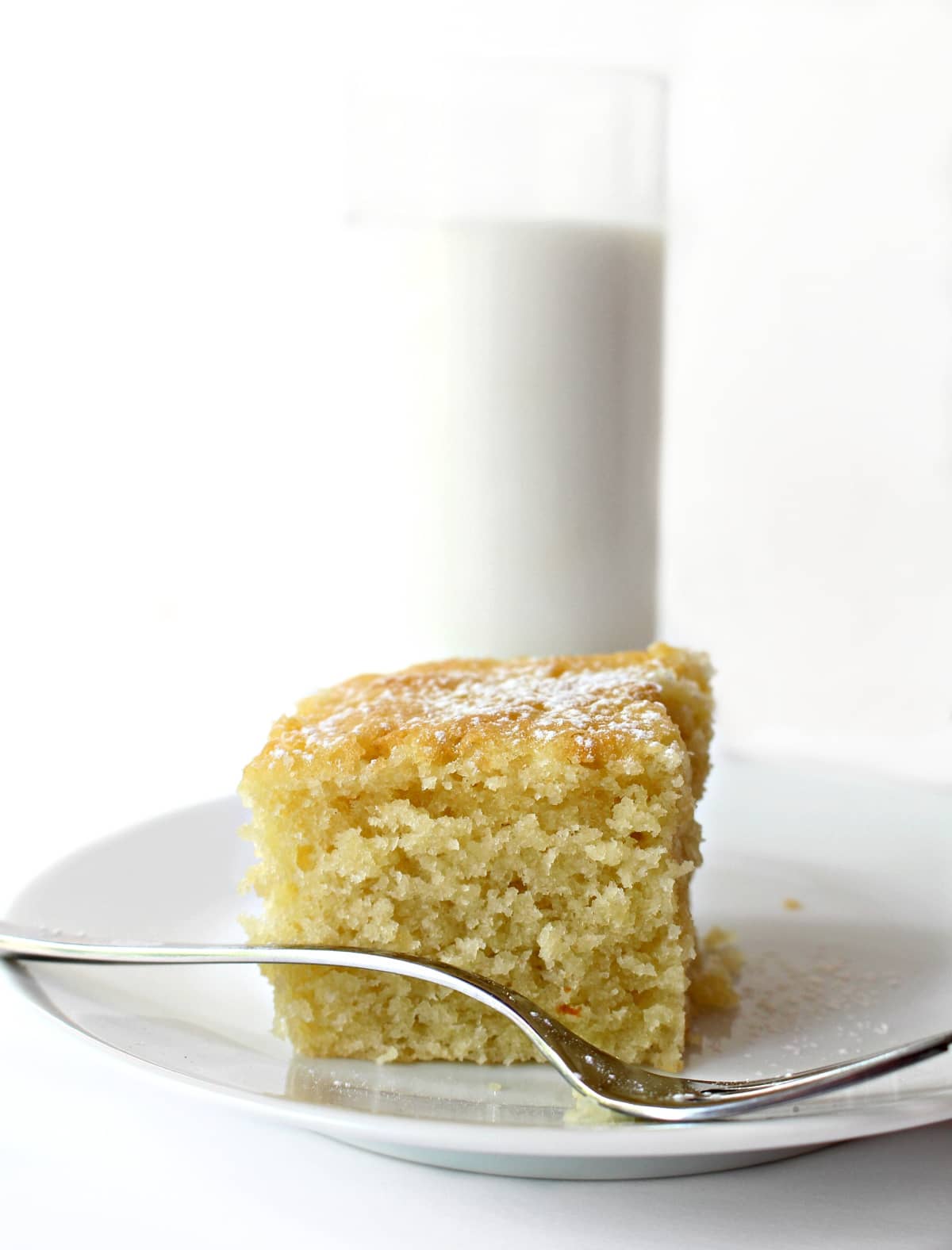 Coconut Milk Snack Cake square on a plate with a fork and a glass of milk in the background.