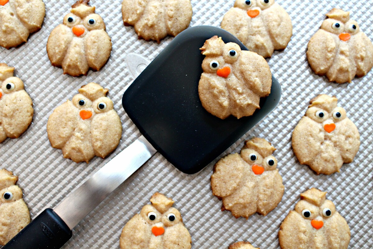 Baked Cinnamon Spritz Owl Cookies being removed from baking sheet with a black spatula.