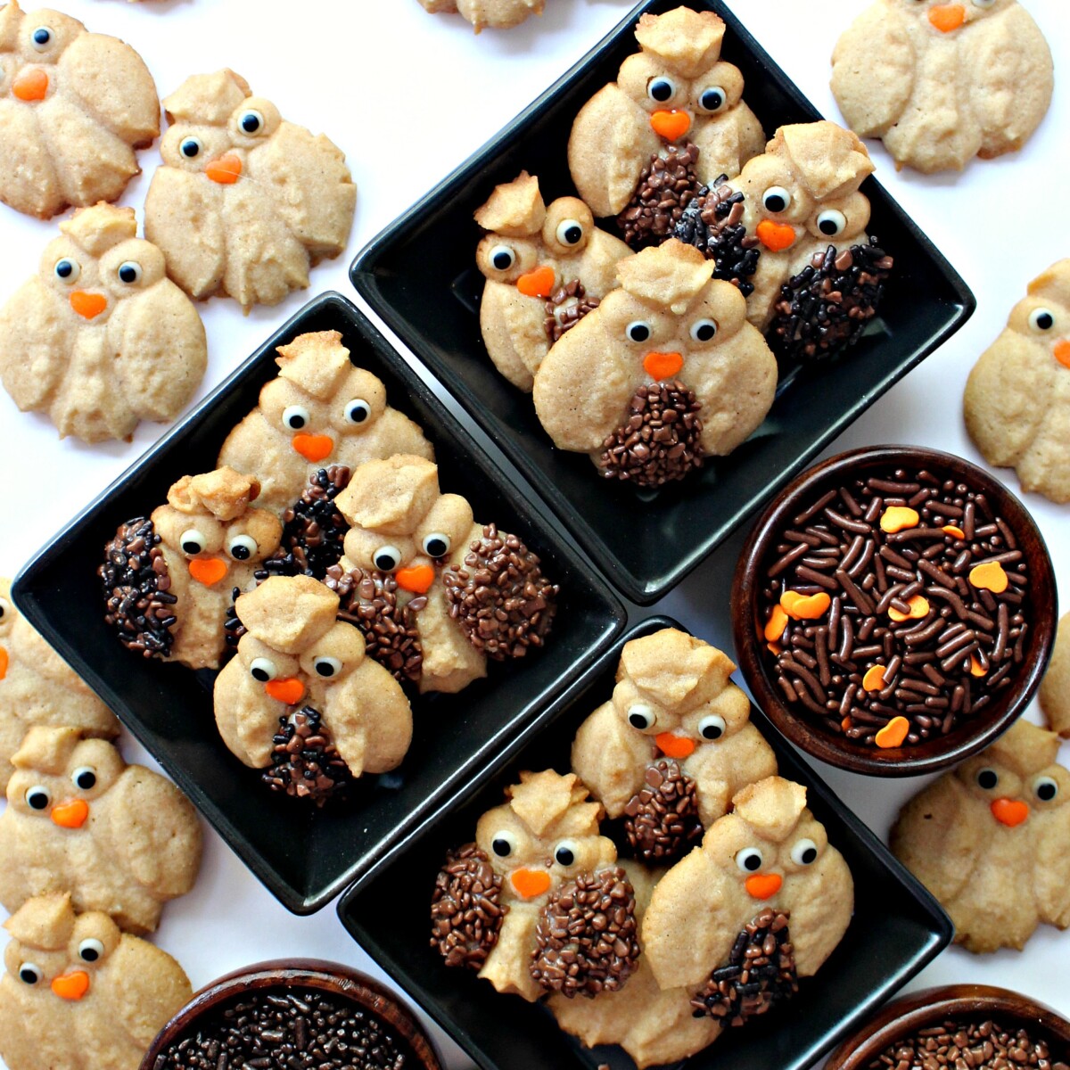 Decorated Cinnamon Spritz Owl Cookies in small black bowls with bowls of decorating sprinkles.