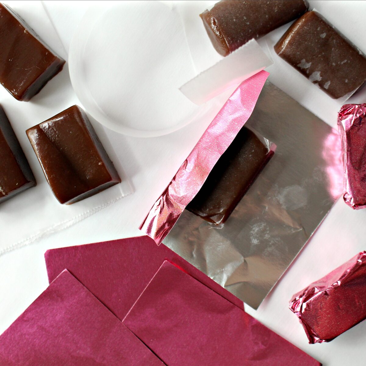 Caramels wrapped in wax paper being wrapped in pink foil.