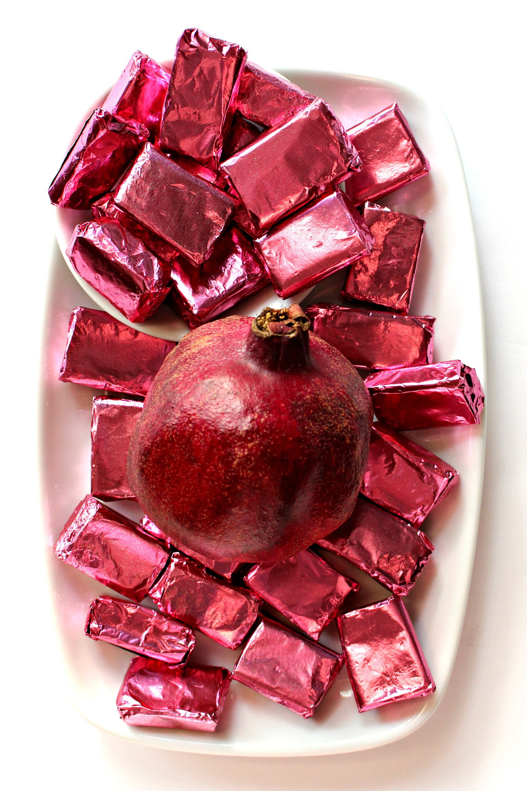 Pomegranate Caramels wrapped in pink foil with a pomegranate on a white serving platter.
