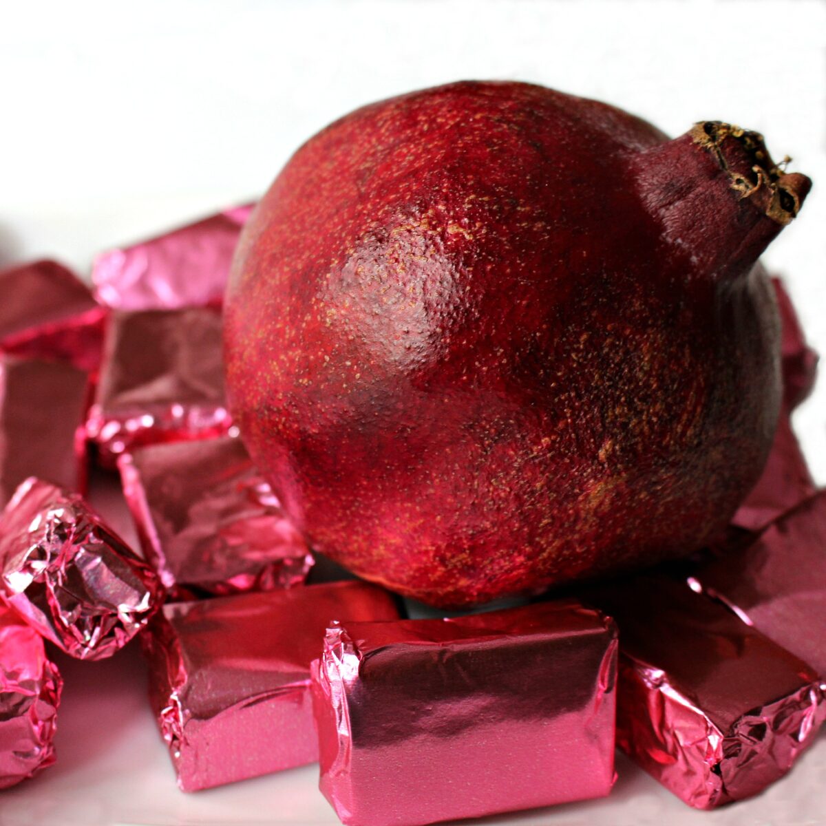A pomegranate surrounded by Pomegranate Caramels wrapped in pink foil.