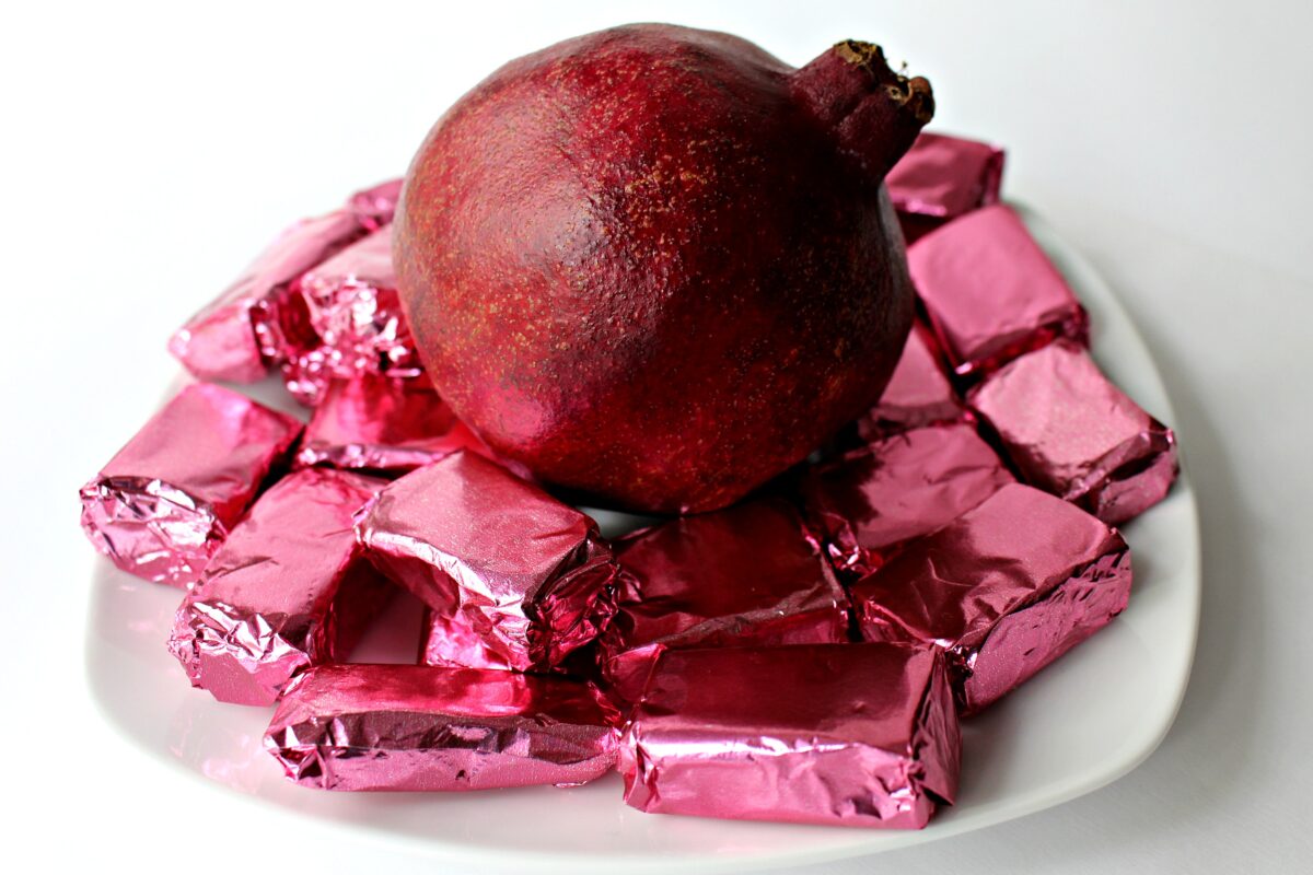 Caramels in pink foil and a pomegranate on a serving plate.