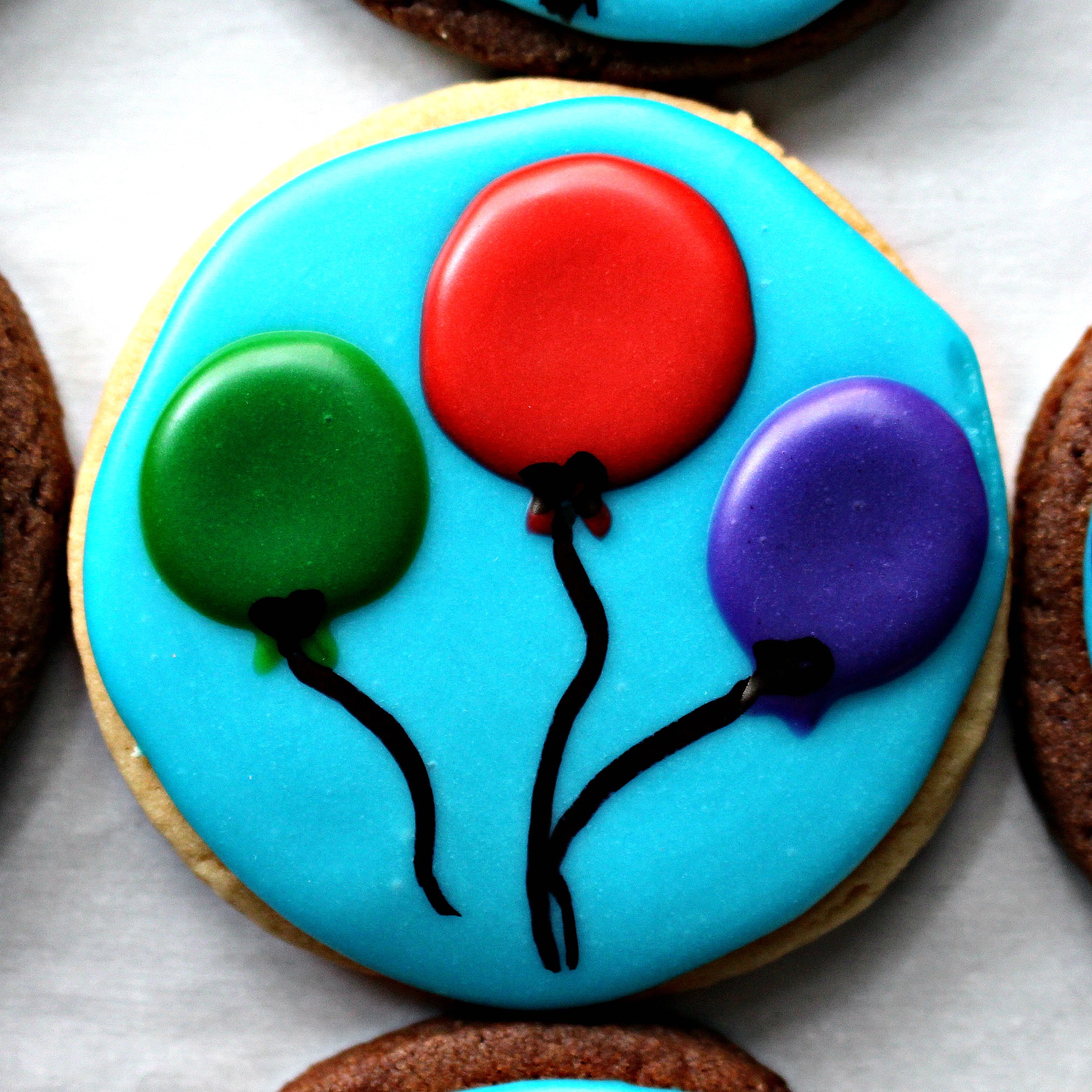 Closeup of round sugar cookie decorated with light blue icing and three balloons.